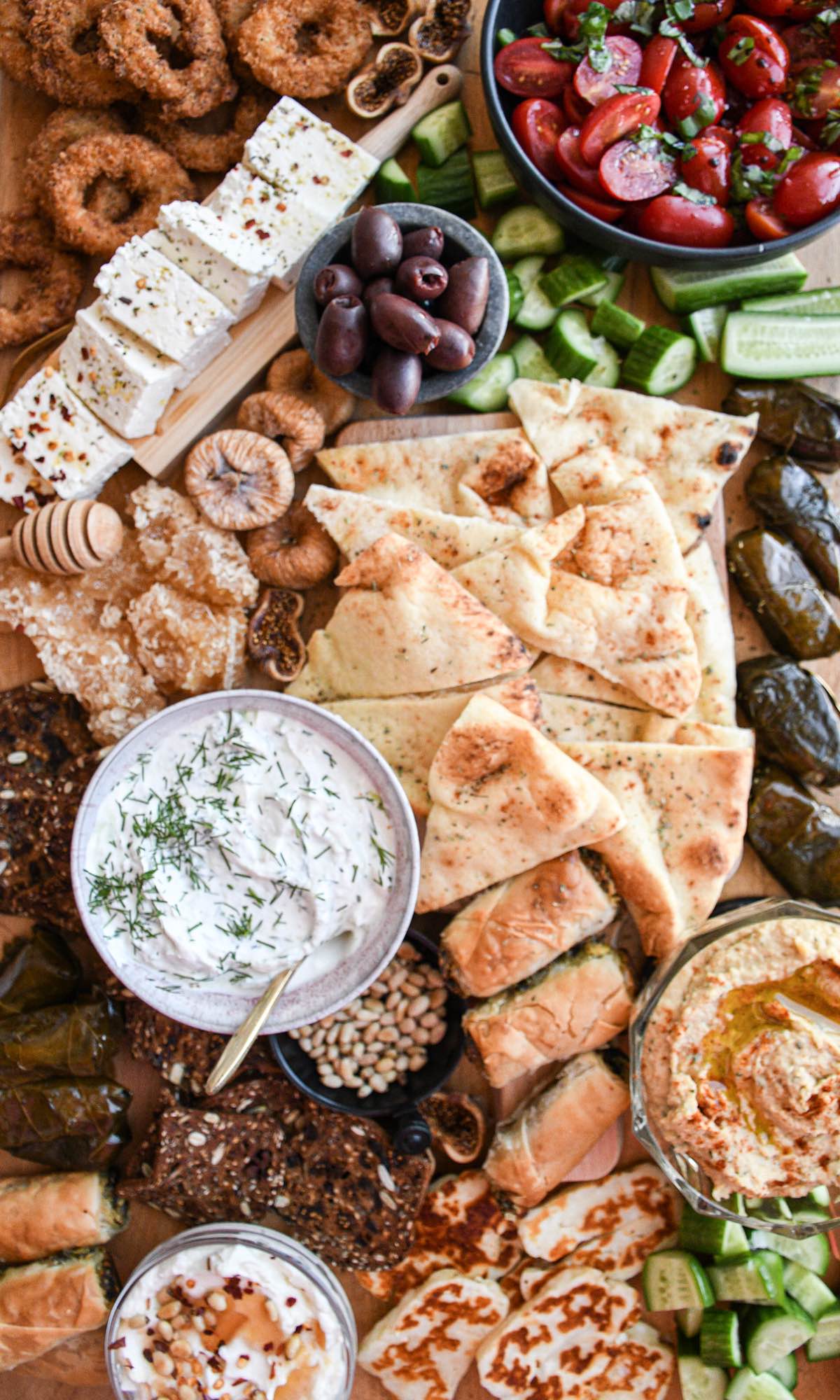 greek mezze board with pita bread, tzatziki, dolmades, halloumi, figs, and sliced feta cheese.