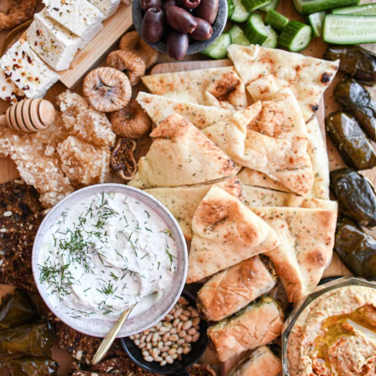 greek mezze board with pita bread, tzatziki, dolmades, halloumi, figs, and sliced feta cheese.