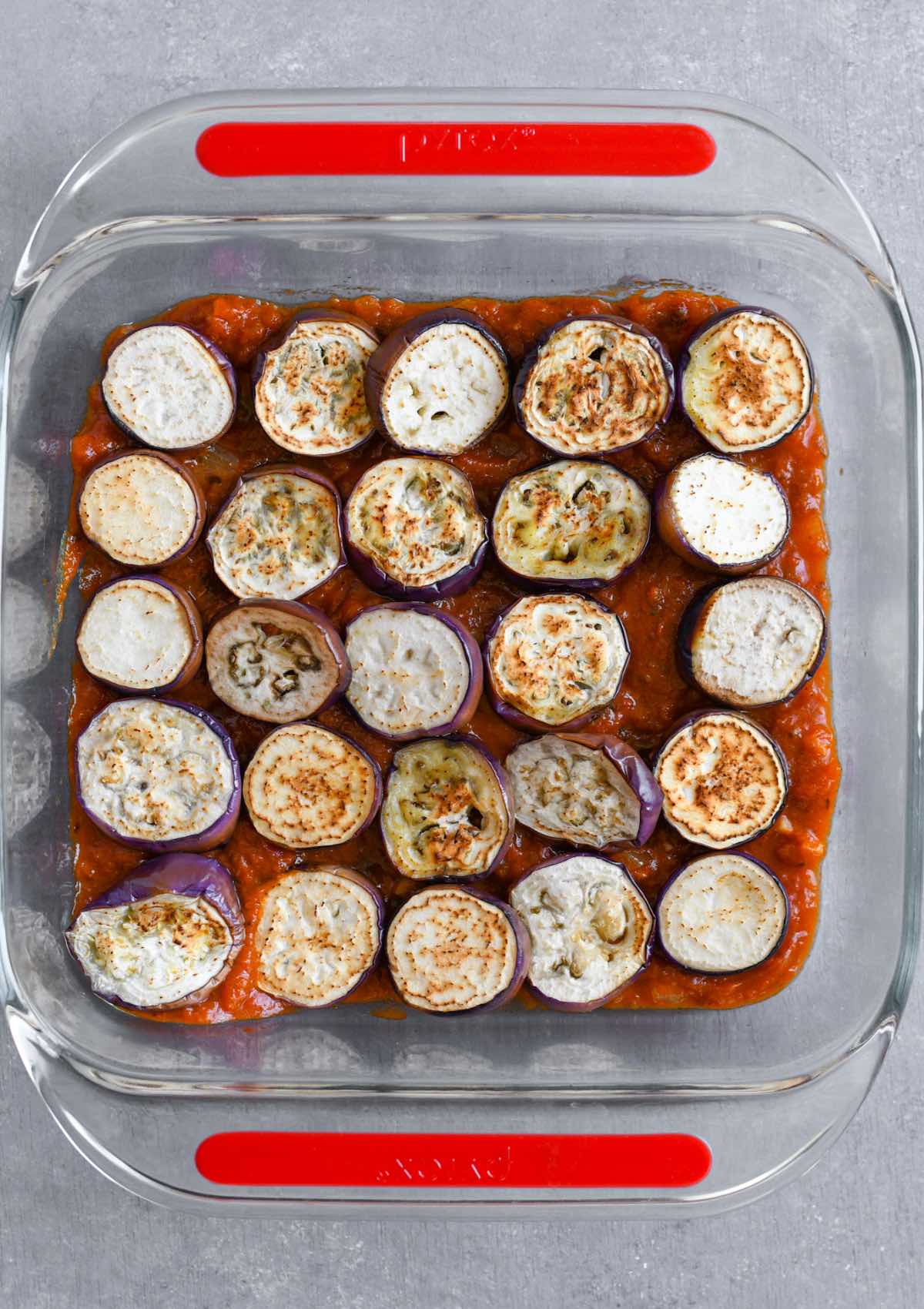 cooked eggplant slices on top of tomato sauce in a baking dish. 