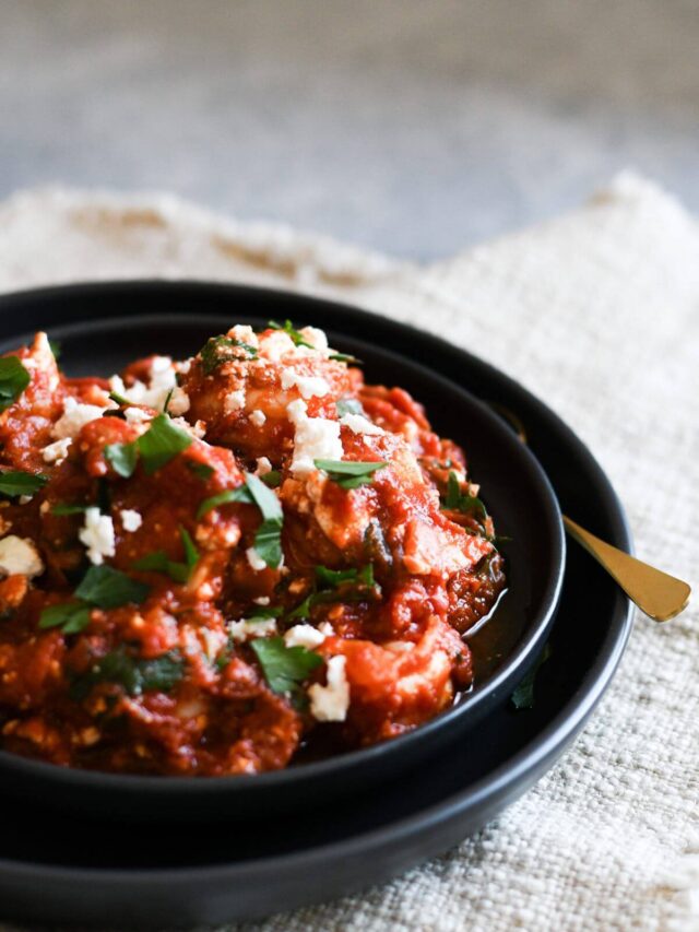 shrimp saganaki with tomato sauce, feta, and Italian parsley in a black bowl.