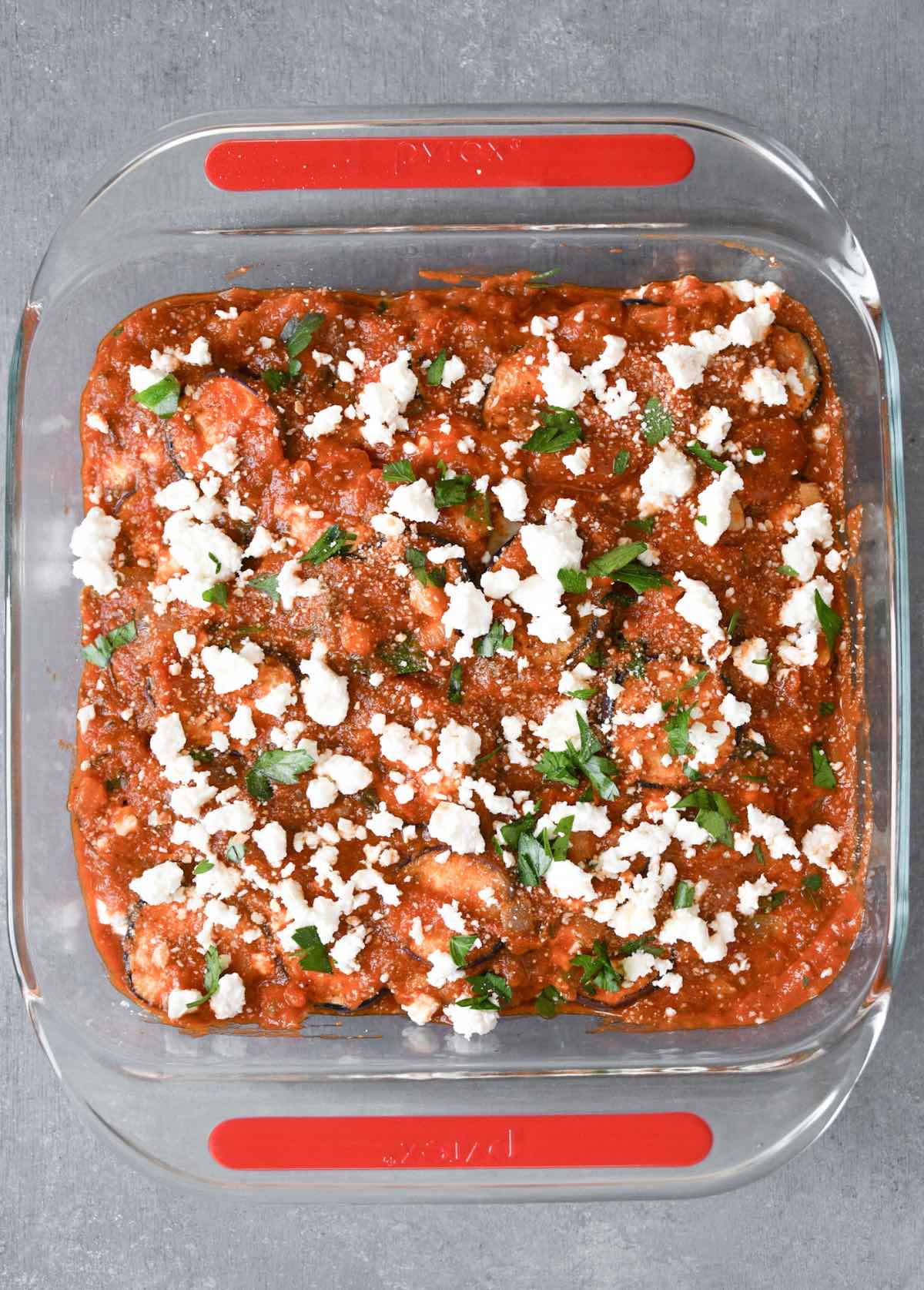 layers of cooked eggplant, tomato sauce, feta and parsley in a baking dish.