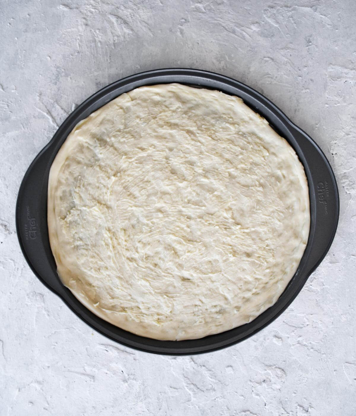 homemade pizza dough stretched out in a 12" pizza pan.