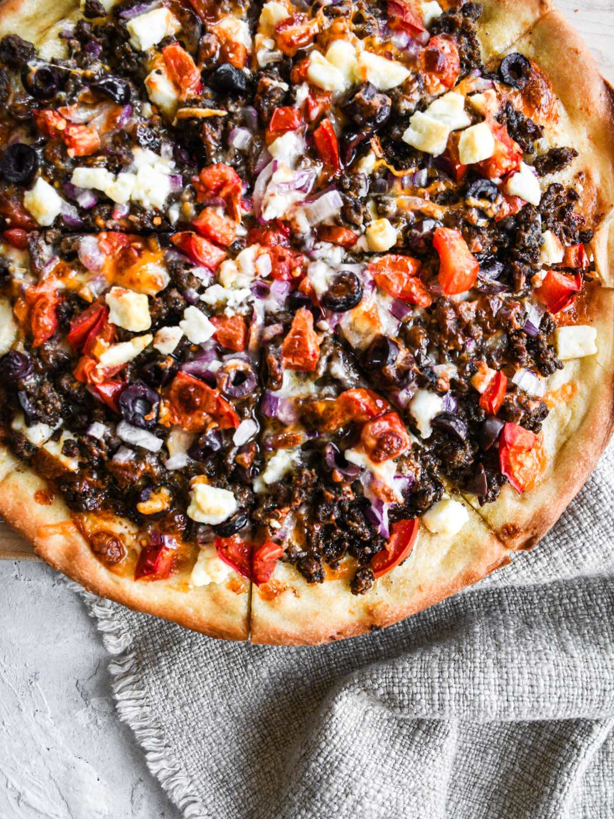 homemade greek pizza with garlic butter, black olives, tomatoes, red onions, feta, and shredded cheese baked in the oven.