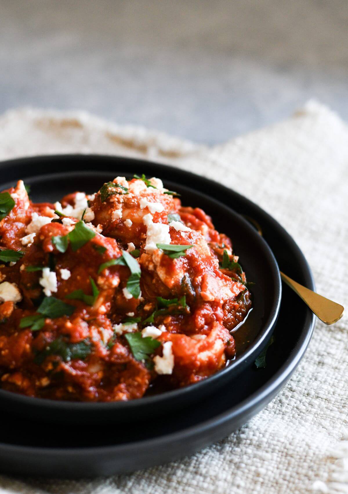 shrimp saganaki with tomato sauce, feta, and Italian parsley in a black bowl.