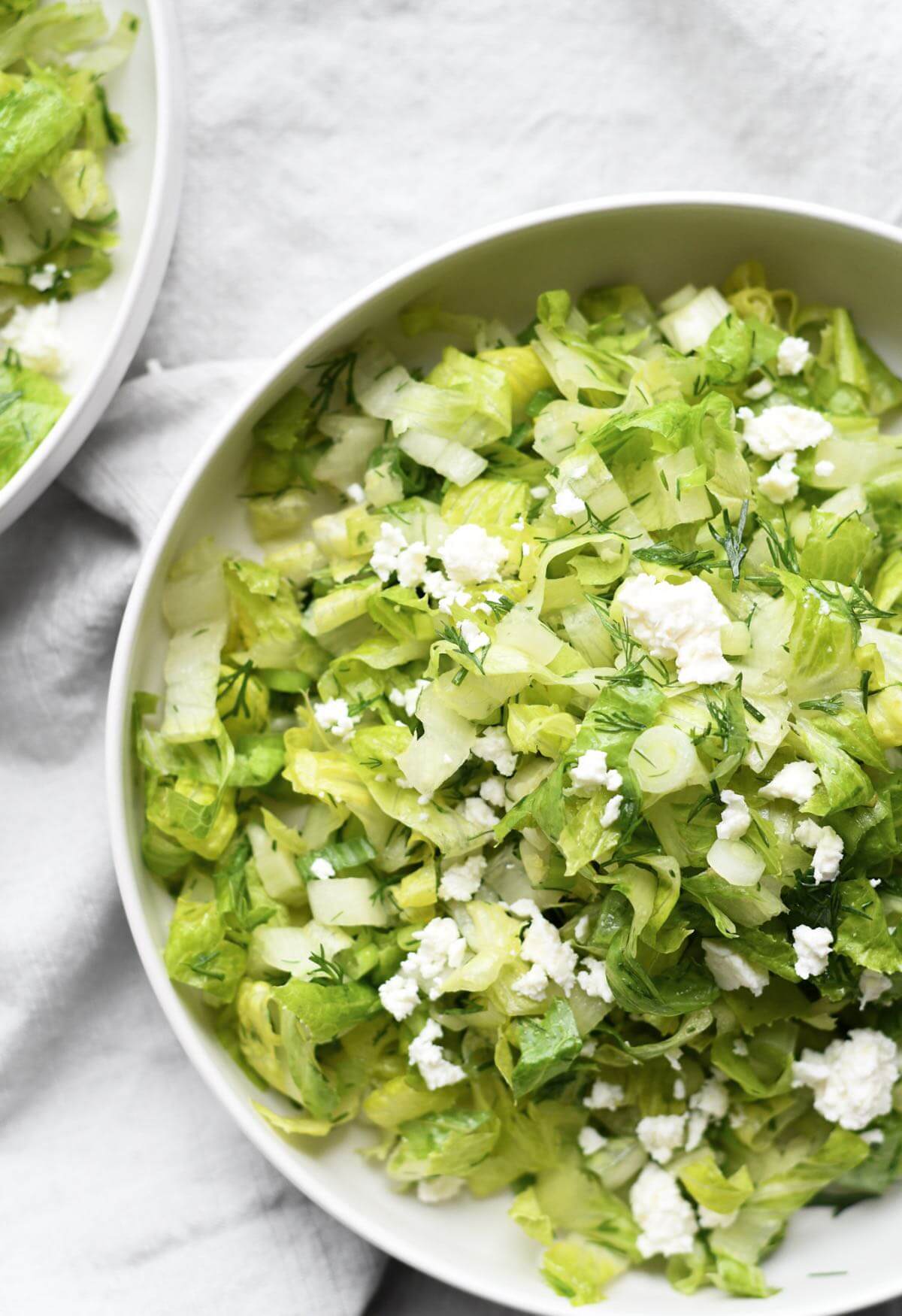 marouli salad with thinly sliced romaine heats, fresh dill, scallions and crumbled feta cheese in a white bowl.