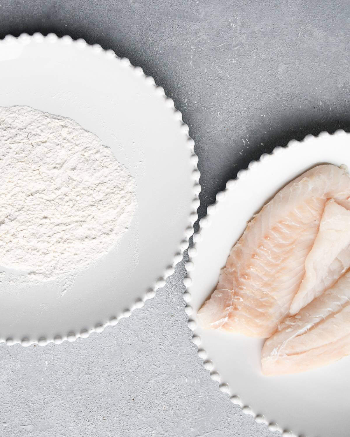 flour on a white plate and two pieces of fresh cod on a white plate.