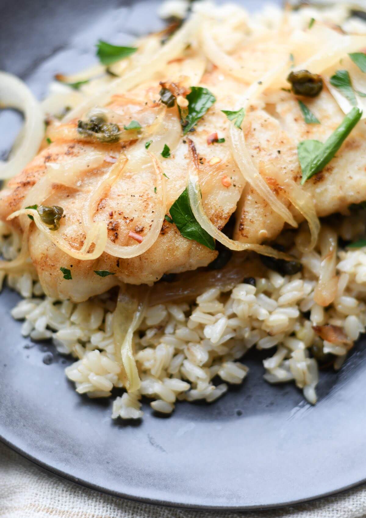 a piece of pan seared greek cod with caramelized onions, capers, and white wine served with brown rice.