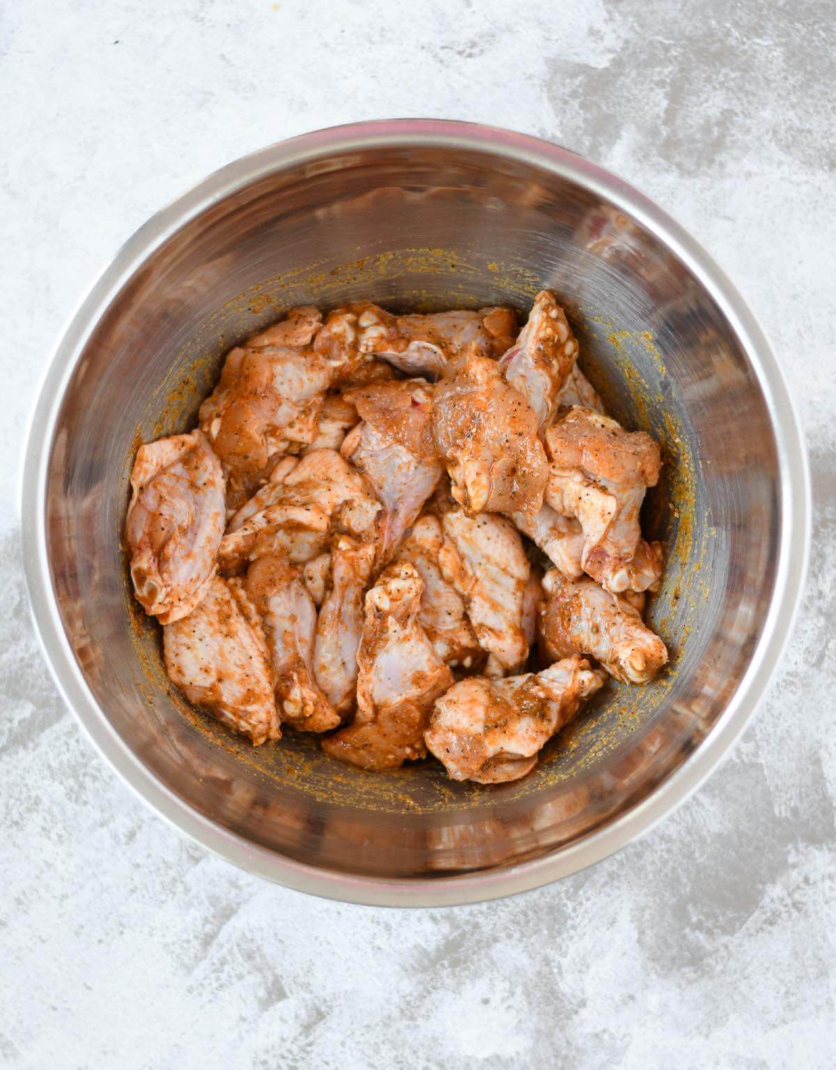 chicken wings marinated in Greek seasonings in a large bowl.