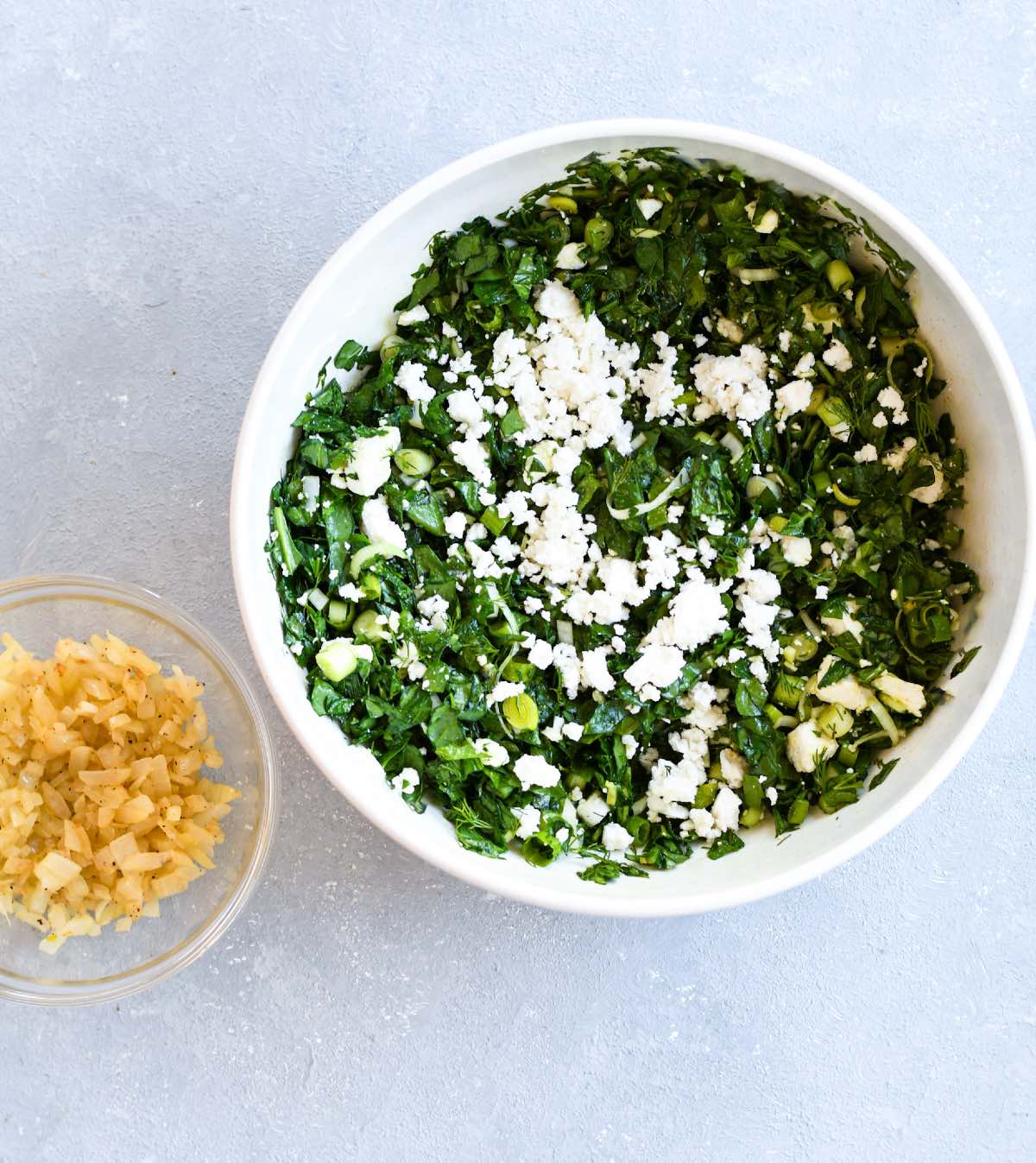 spinach, leek, fresh herbs, feta, rice and parsley in a large bowl. Sautéed onions in a separate bowl.