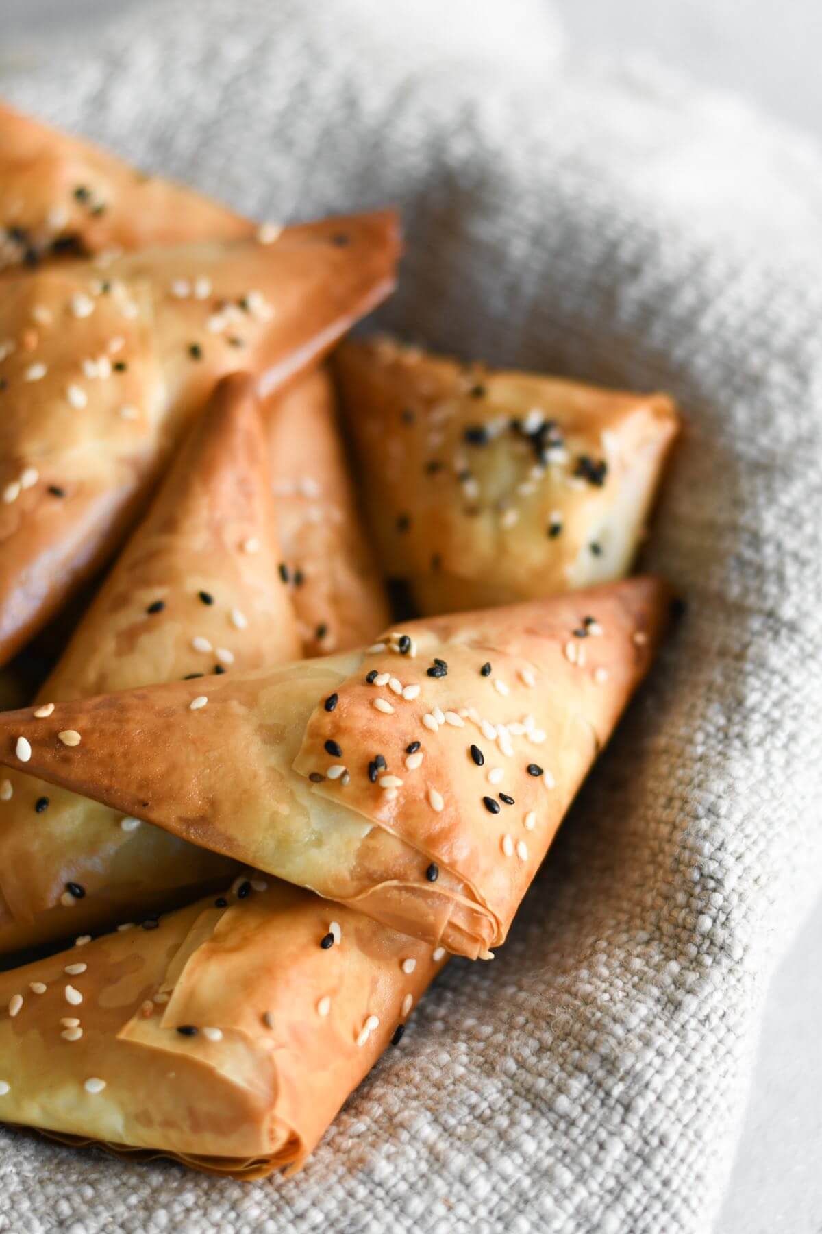 spanakopita triangles with black and white sesame seeds in a bowl.