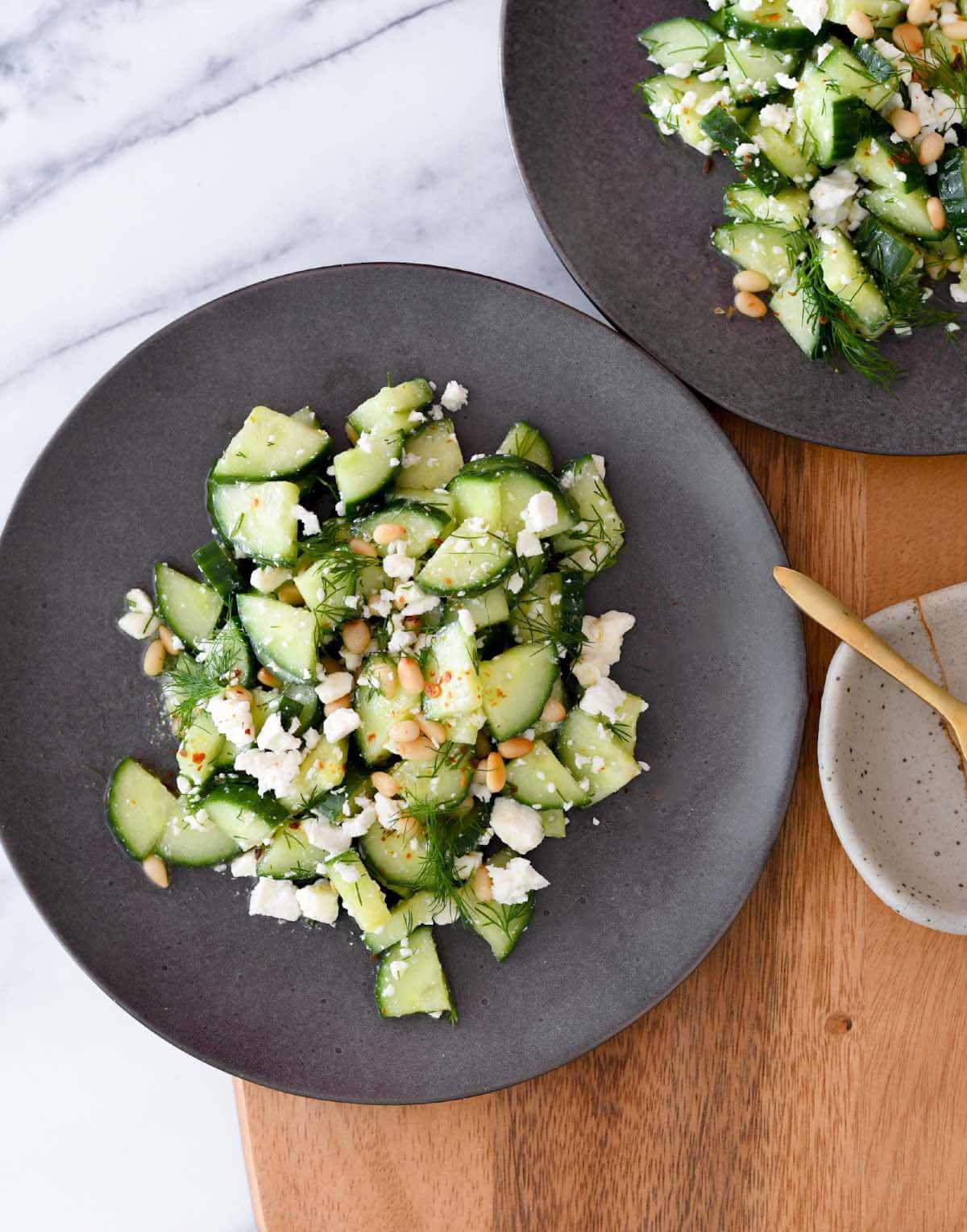 cucumber dill salad with crumbled feta cheese and honey dijon dressing on a black plate.