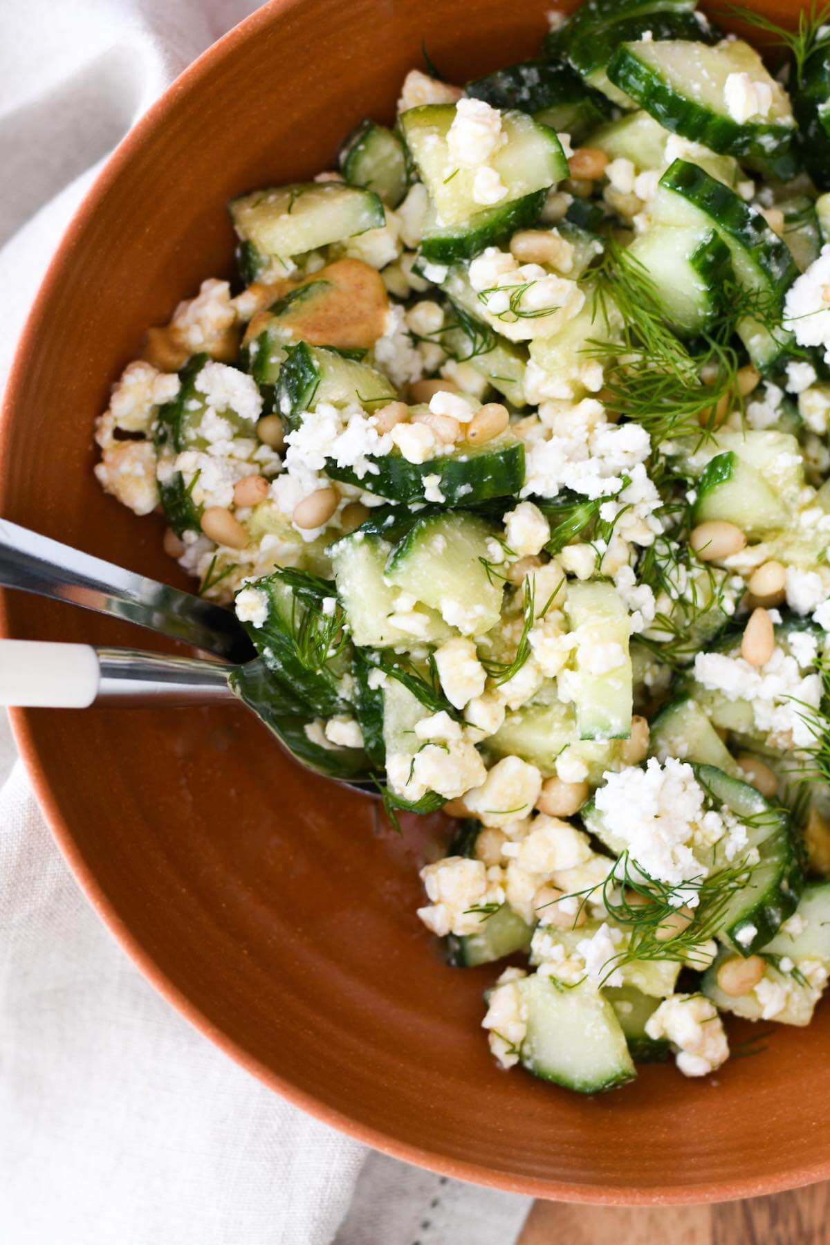 diced cucumbers with crumbled feta cheese, fresh dill, pine nuts and creamy honey mustard dressing in a large bowl.